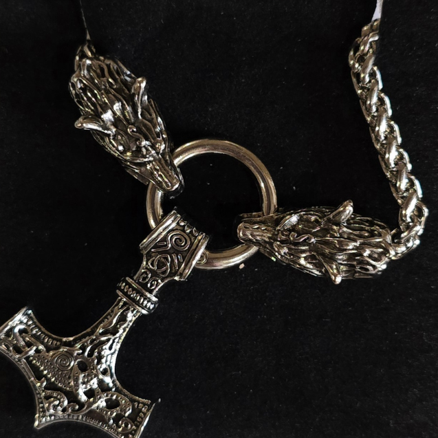 Silver necklace with a Thor's hammer and wolf head design on a black background